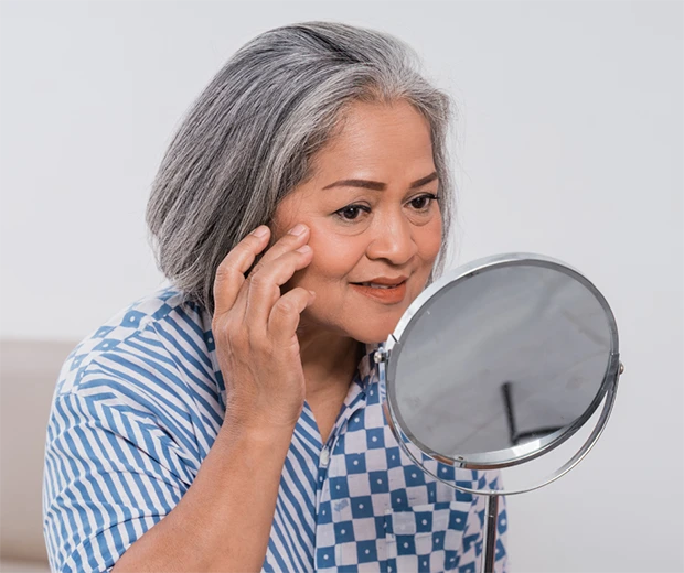 Mature Gray Haired Lady Looking At Facial Wrinkles In the Mirror 